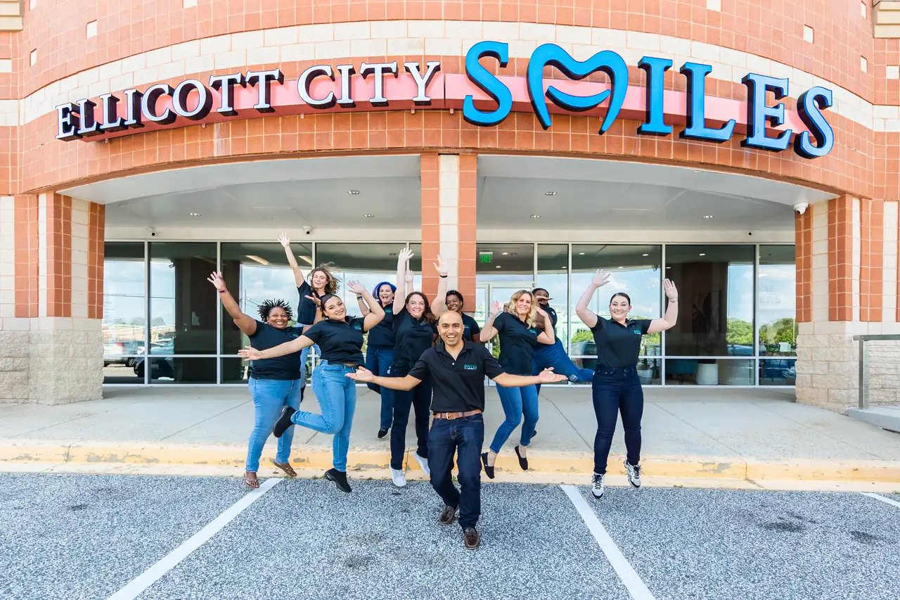 The Ellicott City Smiles team jumping for joy outside the office, under the blue SMILES sign on Baltimore National Pike.