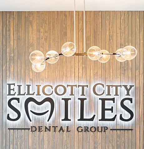 The backlit Ellicott City Smiles Dental Group sign on the wood-slat wall inside the office.