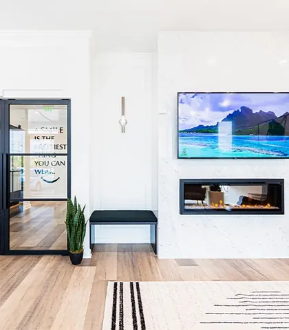 The waiting room, with a fireplace, a wall-mounted screen and a glass door to the clinic.