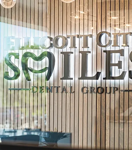The backlit Ellicott City Smiles sign on a wood-slat wall, under a globe chandelier.